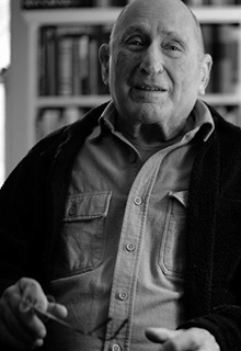 A black and white image of a white man sitting in front of a book shelf smiling