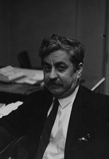 A black and white image of a man in a suit and tie sitting at a desk