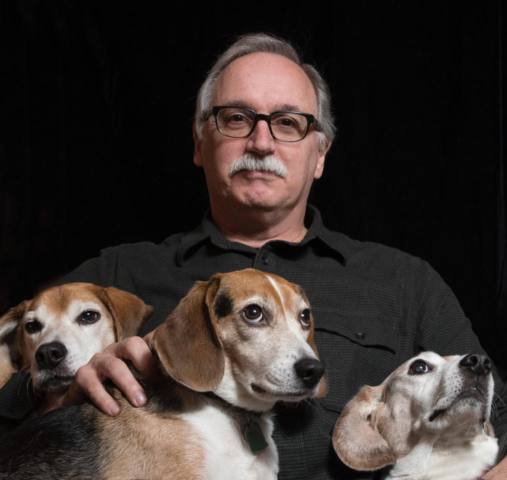 A picture of a man staring at the camera with three dogs